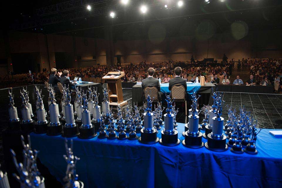 View from behind a trophy table on stage at a tournament with students and an audience View from behind a trophy table on stage at a tournament with students and an audience