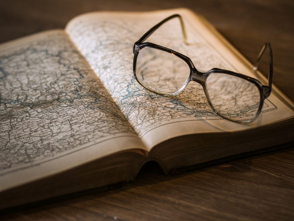 A book open to a spread of a map. There is a pair of glasses on top of the book
