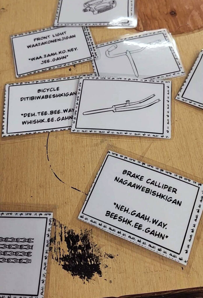 Flashcards on a table. on one side shows a illustration of a bike part. on the other side is the translation in Anishinaabemowin or English.